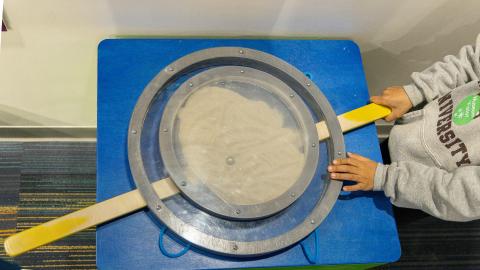 a child uses a tabletop exhibit with sand and a lever