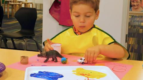a young boy uses toys as paintbrushes
